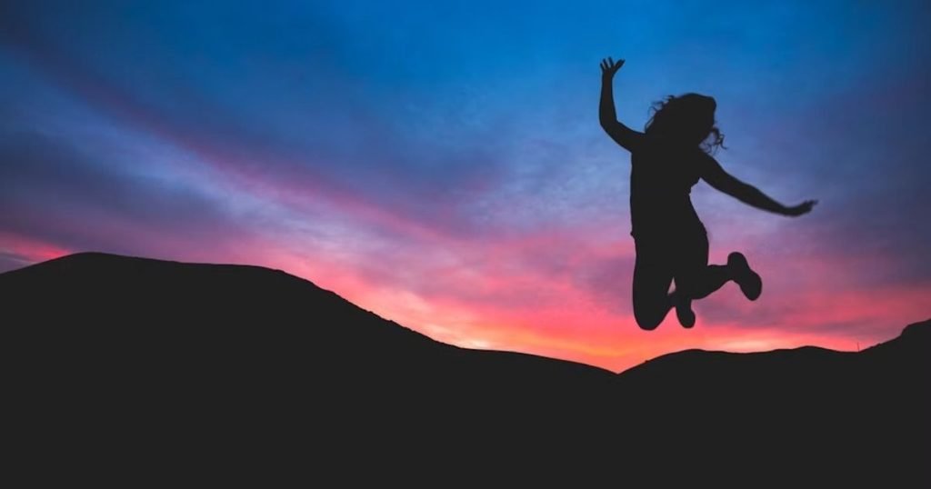 楽しそうに飛び上がっている女性のシルエットがうつる夕暮れ時の写真